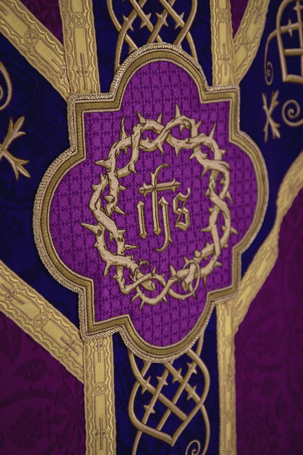 An IHS inside a crown of thorns, in a gold quatrefoil on a violet chasuble