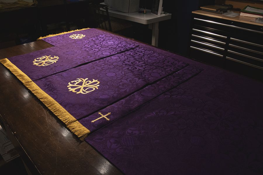 Violet paraments laid out on our workroom table, with gold monograms, a small cross and gold fringe