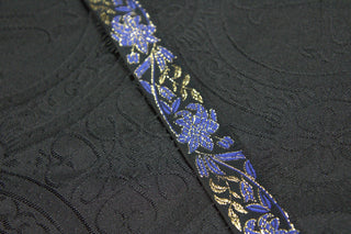 Royal blue gold and black floral jacquard trim displayed on black ecclesiastical brocade fabric