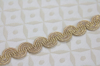Close-up of textured metallic gold woven gimp braid trim with flexible curved construction