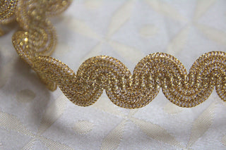 Close-up of textured metallic gold woven gimp braid trim with flexible curved construction