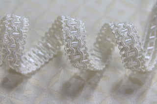 Close-up of 1/2 inch ivory woven gimp braid with raised decorative pattern