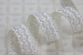Close-up of 1/2 inch white and ivory woven gimp braid with raised decorative pattern