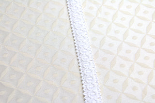 White narrow gimp braid displayed on light ecclesiastical brocade fabric close up