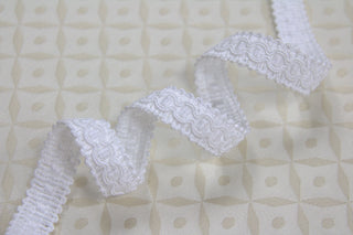 White narrow gimp braid displayed on light ecclesiastical brocade fabric