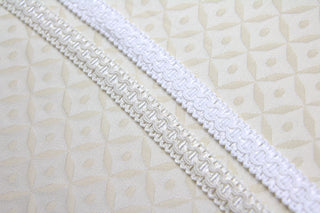 Close-up of 1/2 inch white and ivory woven gimp braid with raised decorative pattern