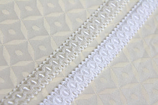 White and ivory narrow gimp braid displayed on light ecclesiastical brocade fabric