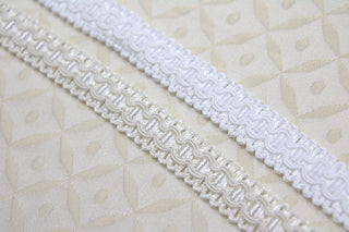 White and ivory narrow gimp braid displayed on light ecclesiastical brocade fabric