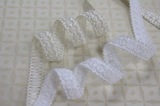 Ivory and White narrow gimp braid displayed on light ecclesiastical brocade fabric