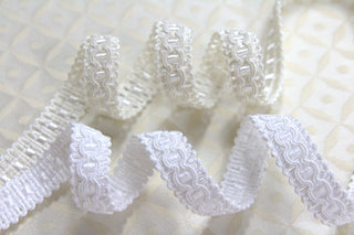 Ivory and White narrow gimp braid displayed on light ecclesiastical brocade fabric