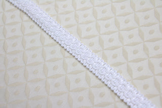 White narrow gimp braid displayed on light ecclesiastical brocade fabric