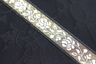 Close-up of white rose jacquard ribbon trim with gold metallic ground and black edging on black ground