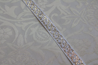 White and gold narrow jacquard trim displayed on white ecclesiastical brocade fabric