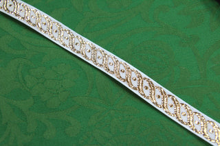 Close-up of white jacquard ribbon with repeating metallic gold scroll and oval design