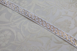 White and gold narrow jacquard trim displayed on white ecclesiastical brocade fabric
