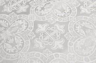 Close detail of an ornamental cross and scrolling floral quatrefoils woven into Chartres white brocade.