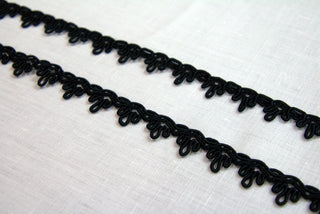 Two lengths of black crown gimp braid laid on white linen