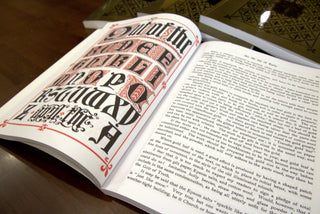 Open book showing an illuminated red and black alphabet plate for lettering church texts and banners