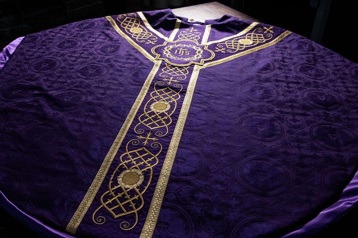 A violet chasuble laid out with a gold orphrey and an IHS in a crown of thorns