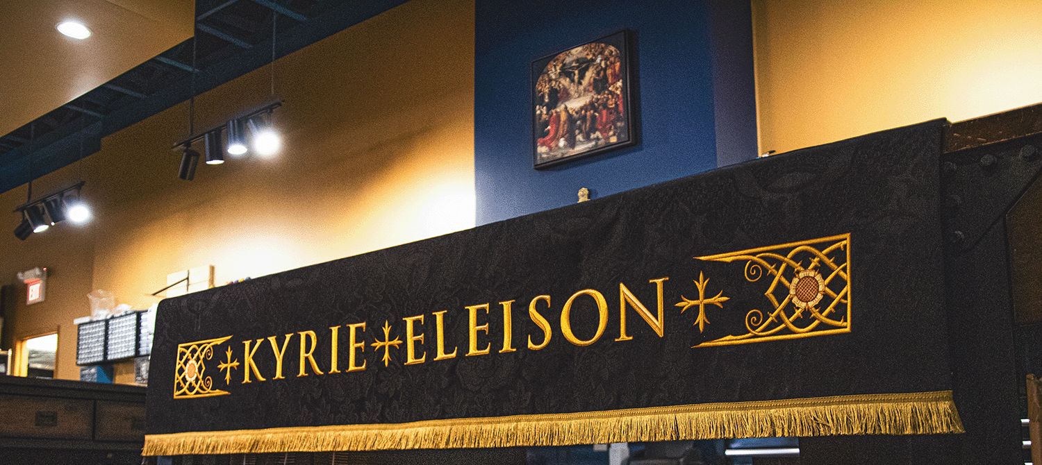 A black Kyrie Eleison hanging with gold lettering and fringe in our workroom