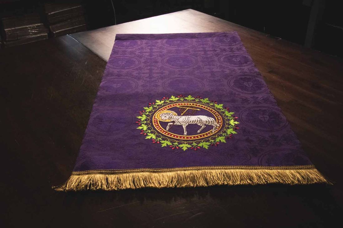 A violet hanging laid flat, with the Lamb of God in a wreath and gold fringe