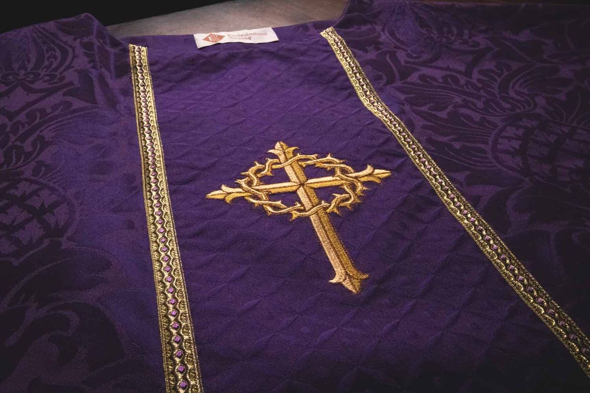 A gold cross wreathed in thorns on violet brocade between gold galloon