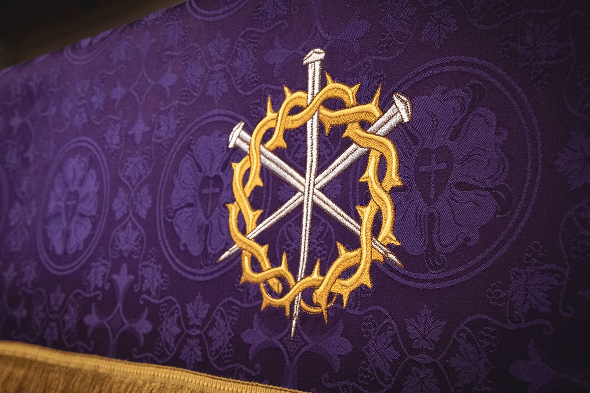 Three crossed nails inside a gold crown of thorns on violet brocade