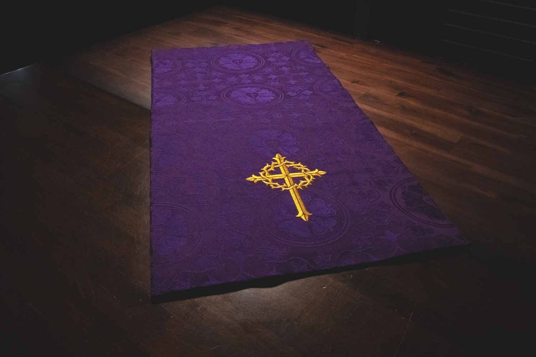 Violet brocade laid flat, with a small gold cross wreathed in thorns near one end